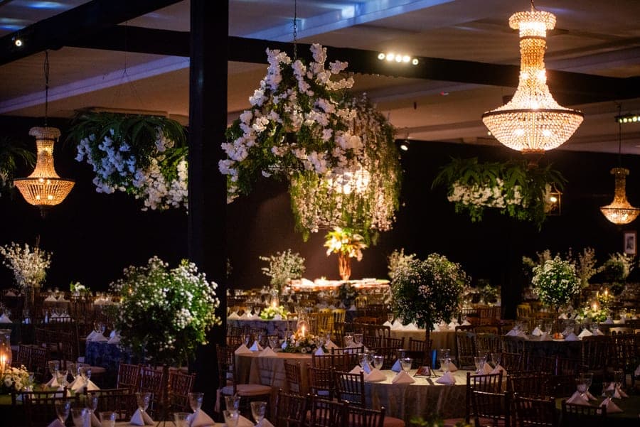 Salão de gala decorado com lustres de cristal e arranjos de flores brancas suspensos