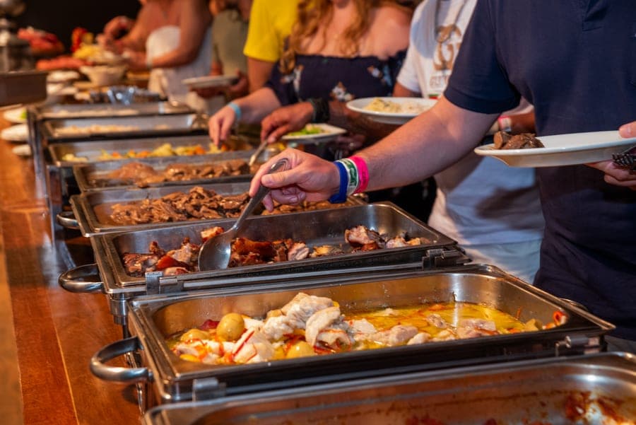 Hóspedes se servindo no buffet da ceia, com travessas quentes de carnes e peixes