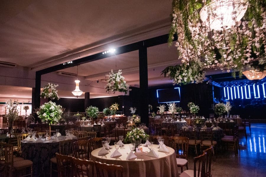 Salão do Réveillon montado com mesas postas, arranjos florais e palco iluminado ao fundo